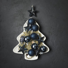 Christmas blue glass balls in plate shape of fir tree on black. Xmas greeting card.