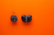Ripe plum and ugly accreted prunes on an orange background. Place for text. Fused fruits. Funny, unnormal vegetable or food waste concept