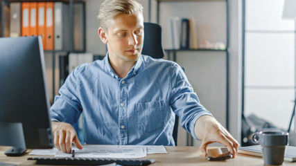 Canvas Print - Businessman Sitting at His Desk Works on Desktop Computer in the Stylish Office, Picks up Smartphone, Important Email, Message, Incoming Business Call.