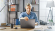 © Gorodenkoff - Creative Entrepreneur Sitting at His Desk Works on a Laptop in the Stylish Office, Uses Software for Social Media Apps, Emailing Business Associates, Reading News, Browsing through Internet