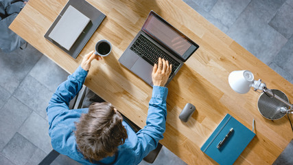 Wall Mural - in the office businessman sitting at the wooden desk works on a laptop in his home office. he drinks