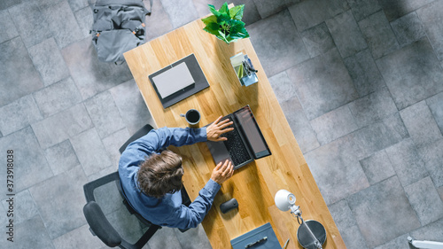Fotomural Top View Shot: Businessman Sitting at the Wooden Desk Works on a Laptop in his Home Office