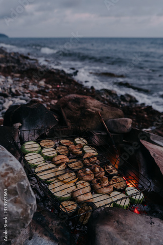 Delicious and healthy food without meat. A variety of vegetables and mushrooms grilled over a fire on a grill. Vegetarian barbecue on the fire on the beach.