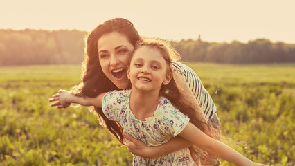 Wall Mural - Happy enjoying mother hugging her playful laughing kid girl in sunset sunny light on summer background in bright yellow colors. Closeup