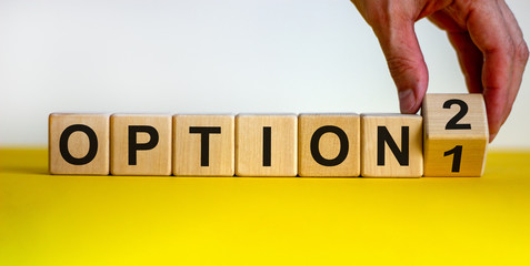 Option 1 or option 2. Hand turns a cube and changes the number '1' to '2' or vice versa. Word option on wooden cubes. Beautiful yellow table, white background. Business concept. Copy space.