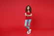 © ViDi Studio - Full length portrait smiling young african american woman girl in casual t-shirt posing isolated on red background. People lifestyle concept. Mock up copy space. Holding hands crossed, looking aside.