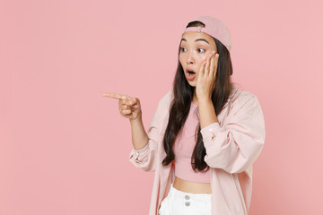 Wall Mural - Shocked young asian woman girl in casual clothes cap posing isolated on pastel pink wall background studio. People lifestyle concept. Mock up copy space. Pointing index finger aside put hand on cheek.