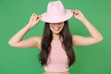 Smiling Young Asian Woman Girl In Casual Pink Clothes Posing Isolated On Green Background Studio Portrait. People Sincere Emotions Lifestyle Concept. Mock Up Copy Space. Covering Eyes With Hat Hiding.