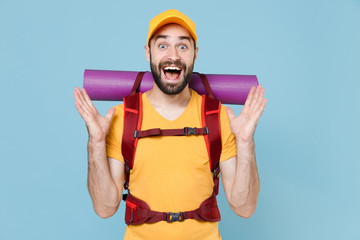 Wall Mural - Amazed traveler young man in yellow t-shirt cap with backpack isolated on blue background. Tourist traveling on weekend getaway. Tourism discovering hiking concept. Keeping mouth open spreading hands.