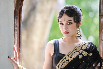 Portrait of beautiful young asian Thai girl. Woman model with kundan jewelry set and traditional hindu India costume black, gold saree and lehenga dress.