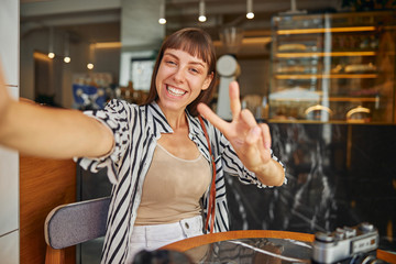 Cheerful young woman photographer with cropped up hand in cafe