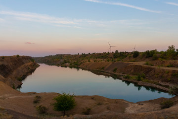 Wall Mural - Wind turbine rises above small lake at the sunset. Renewable electricity generation theme.