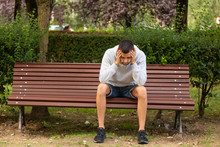 Young Man Sitting On Park Bench With Depressed Attitude Or Loneliness