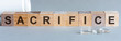the word SACRIFICE written in wooden letters on a grey background