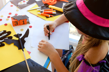 Little girl in a witch costume draws for the holiday of halloween on a light table.