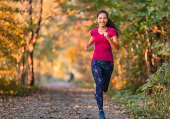 Autumn outdoor active lifestyle. Fit sport woman running in city park at sunset training cardio in nature path. Happy girl exercising outdoors in yellow leaves foliage.