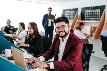 Wall Mural - Mexican man with beard working at computer at office in Mexico and his teamwork at the background