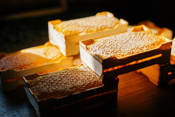 Close-up of honeycombs in wooden frame with full cells of honey sealed with wax on table at dark bee house.