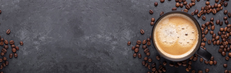 horizontal banner with cup of coffee and coffee beans on dark stone background. top view. copy space