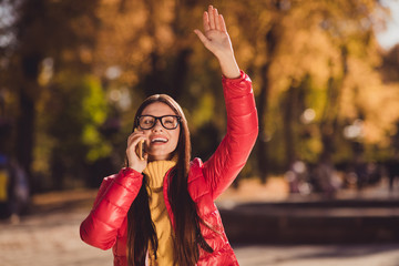 Wall Mural - Photo of positive girl rest relax autumn sunset city center park call smartphone see friend greet want hand wear red jacket coat october outerwear