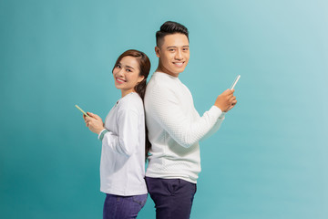 Wall Mural - Smiling young couple friends man woman in casual clothes standing back to back, using mobile cell phones