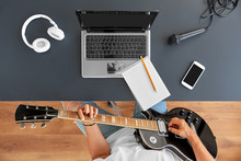 Leisure, Music And People Concept - Young Man Or Musician With Laptop Computer Playing Guitar Sitting At Table