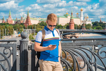 A Young Blond Man Calls On A Mobile Phone With A View Of The Kremlin And The River In Moscow