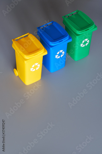 Three color coded recycle bins, isometric picture on geometric paper background with copy-space. Recycling sign on the bins, blue, yellow and green. Waste separation to recycle plastic and glass.
