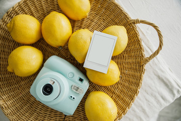 Modern polaroid camera, many lemons, photo frame, wooden background. Top view, tender minimal flat lay style composition. Womens desk, fashion blogger, beauty technology