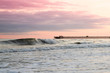 A wave rolling in under a pink and purple sky at sunset. The Apache Pier is visible on the horizon.