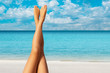 Beautiful long crossed outstretched female tanned legs against the background of the ocean, snow-white sandy beach and blue sky with white clouds