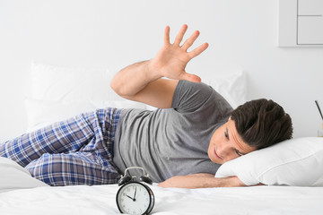 Canvas Print - Young man with alarm clock suffering from insomnia in bedroom