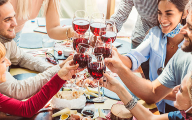 Wall Mural - group of young people enjoying time drinking red wine at restaurant with face mask. new normal conce