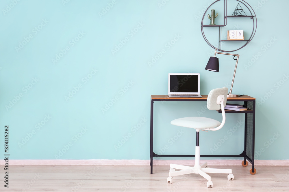 Table with laptop and chair near color wall