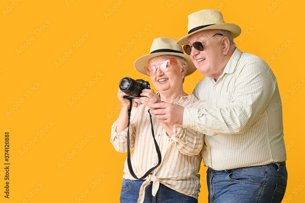 Happy senior couple with photo camera on color background