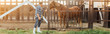 © LIGHTFIELD STUDIOS - panoramic concept of rancher in plaid shirt and rubber boots touching brown horse in corral