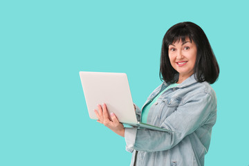 Beautiful mature woman with laptop on color background