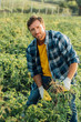 © LIGHTFIELD STUDIOS - farmer in plaid shirt and gloves looking at camera while weeding field
