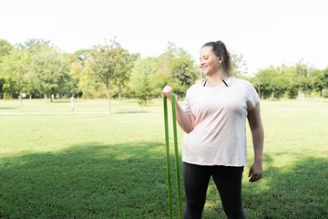 Fat woman stretching with resistance band and listening music at park