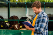 © LIGHTFIELD STUDIOS - rancher in plaid shirt writing on clipboard near cowshed on farm