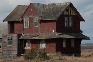 Sticker - Old red house in a dry grassy field under a cloudy sky