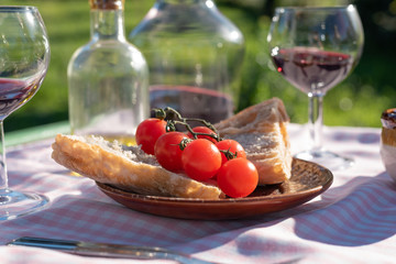 Wall Mural - Tomatoes and bread plate close up with red wine in glass cups and olive oil at sunset. Countryside style and gingham tablecloth