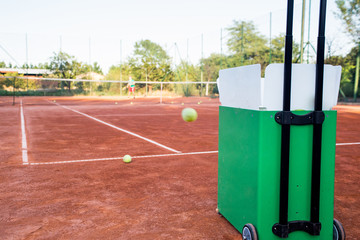 Ball machine on slag tennis court.