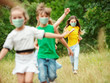 © master1305 - Happy little kids wearing protective face mask jumping and running on meadow, forest. Looks happy, cheerful, sincere. Copyspace. Childhood, pandemic concept. Healthcare, coronavirus pandemic.