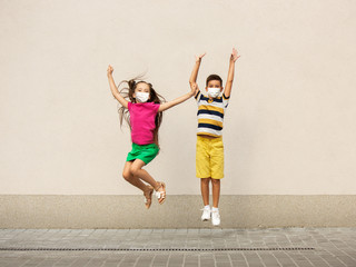 Wall Mural - Happy little kids wearing protective face mask jumping and running on city street. Looks happy, cheerful, sincere. Copyspace. Childhood, pandemic concept. Healthcare, coronavirus pandemic.