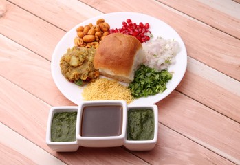 Wall Mural - Dabeli is an Indian snack item served with Pomegranate Seeds and Cilantro in white ceramic plate. with green chutney and tamrind chutney.