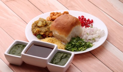 Wall Mural - Dabeli is an Indian snack item served with Pomegranate Seeds and Cilantro in white ceramic plate. with green chutney and tamrind chutney.