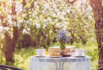 Wall Mural - Springtime in garden. Table set with tea cups, boho reuse jar vase with forget me not flowers( Myosotis) and small stack of books. Summer relax readings concept.