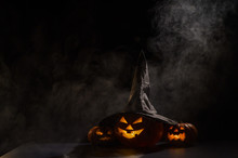 Three Jack O Lanterns Glow In The Dark Amidst The Fog. Halloween Pumpkin In A Witch Hat.