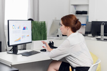 A young businesswoman is preparing for a presentation on a computer, sitting in a spacious, bright open space office.